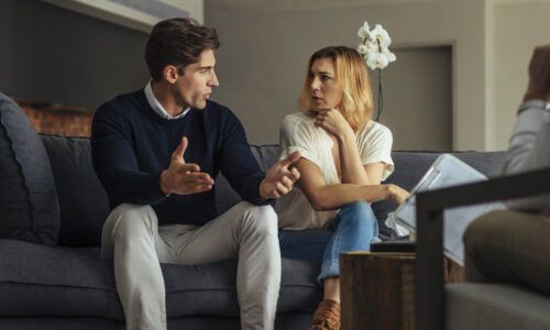 Couple arguing during therapy session with psychologist. Man and woman sitting on couch and talking while psychologist listening them.